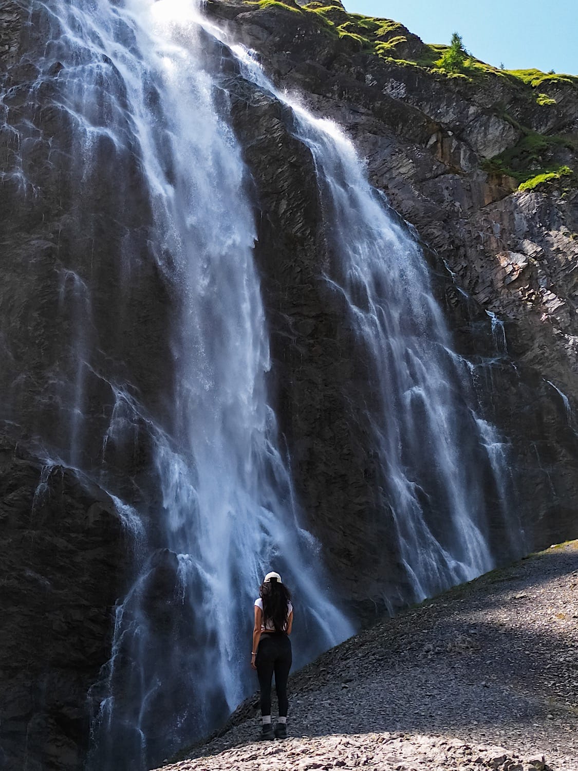 Woman standing at the base of Engstligenfälle, dwarfed by the waterfall cascading down the cliff face