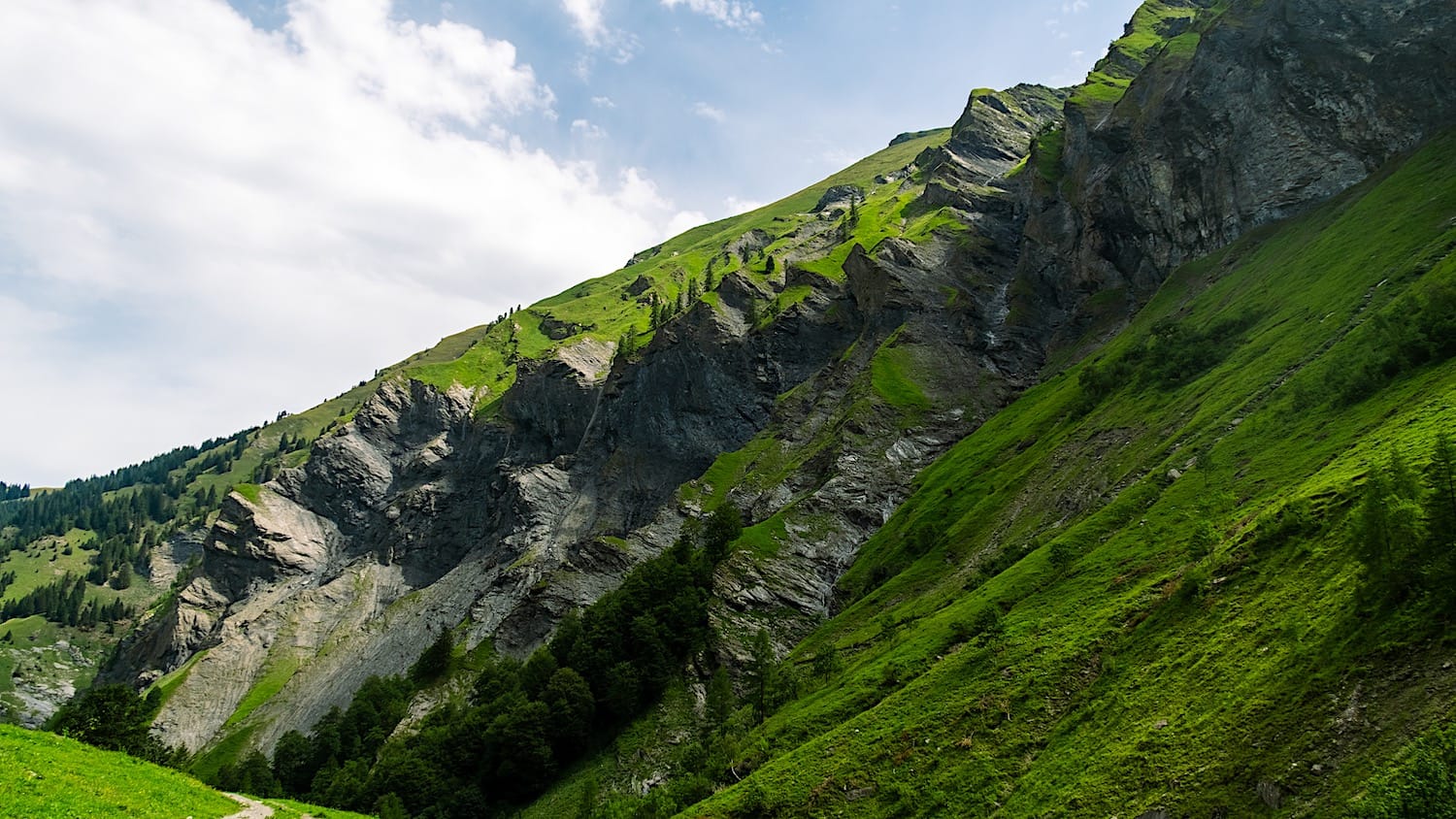 Steep grassy mountainside with exposed rock layers along the trail up to the Waterfall-Arena Batöni
