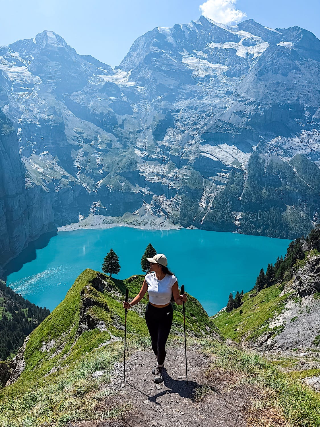 Woman with hiking poles standing in front of a blue lake surrounded by mountains