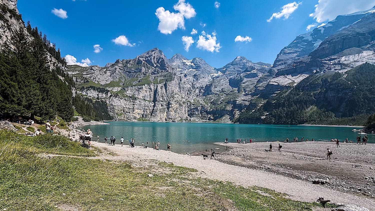 Crowds at the shore of a blue lake. Mountains on the background.
