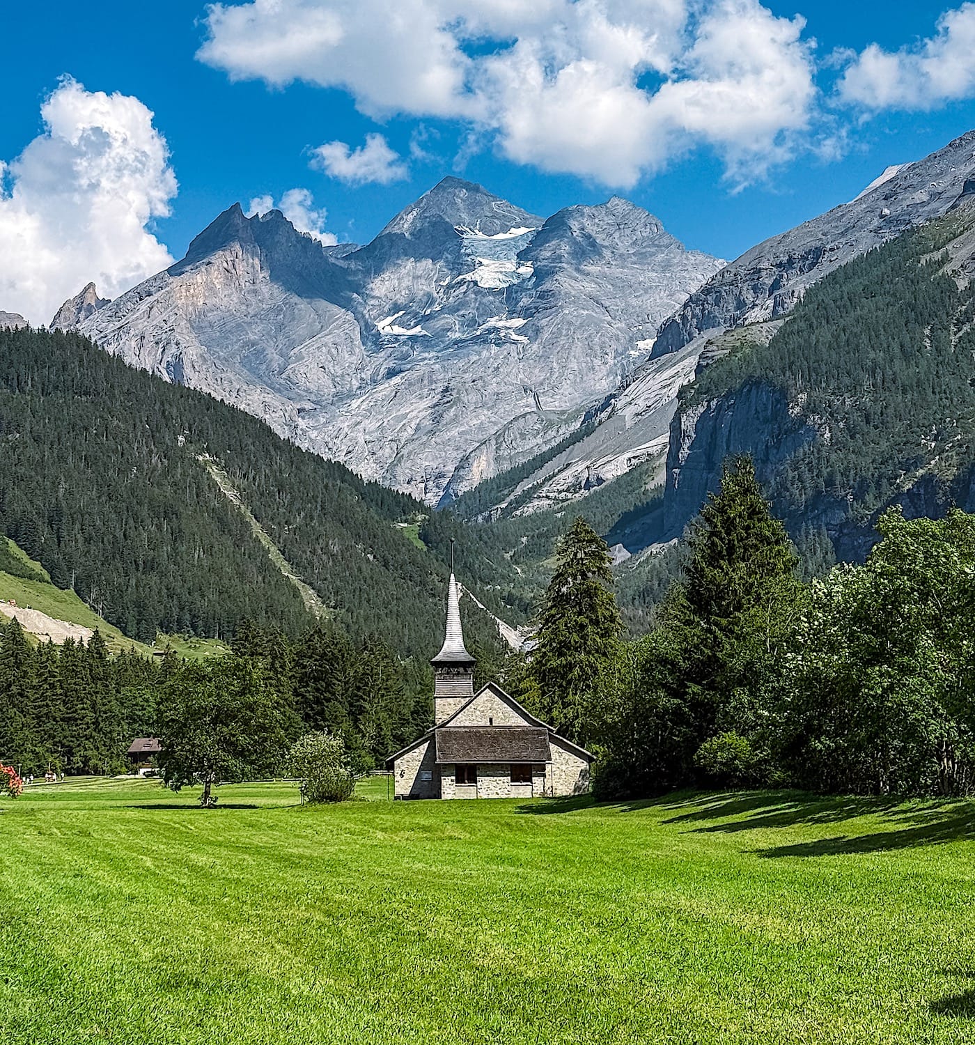 A church on a meadow in front of a distant mountain and a forest below it