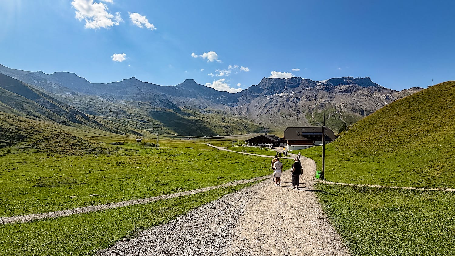 Alpine meadow at Engstligenalp with a mountain hut and hikers on the gravel path, peaks in the background