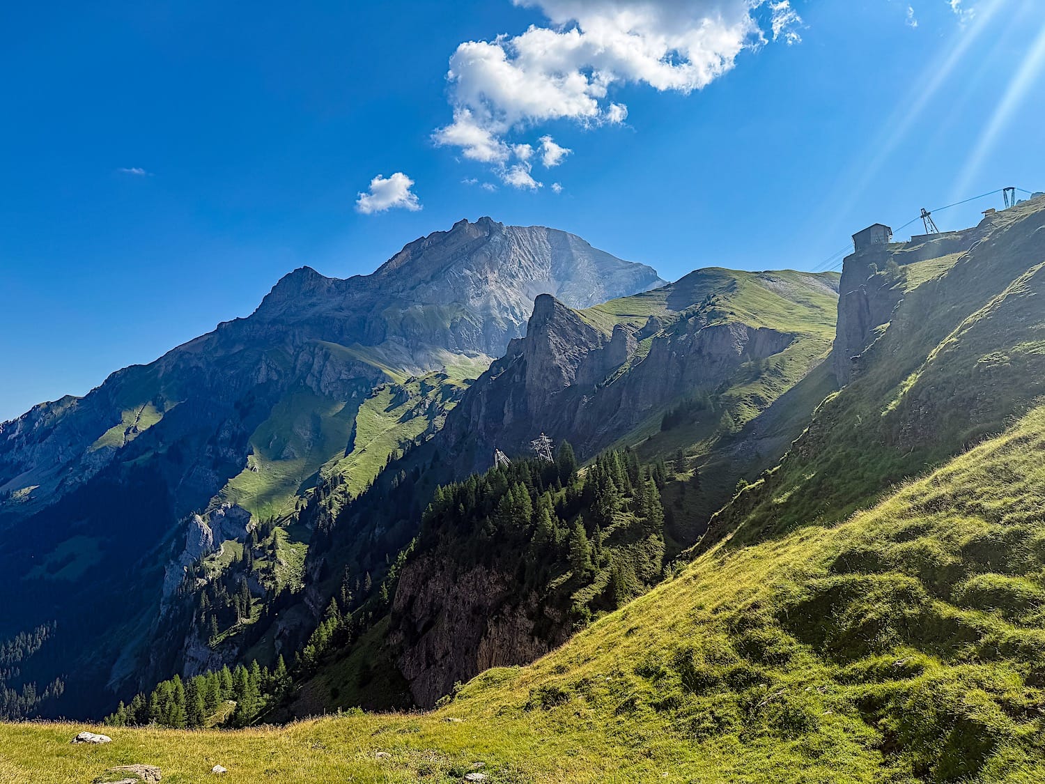 Mountain landscape with the gondola station visible on the cliff edge above the trail