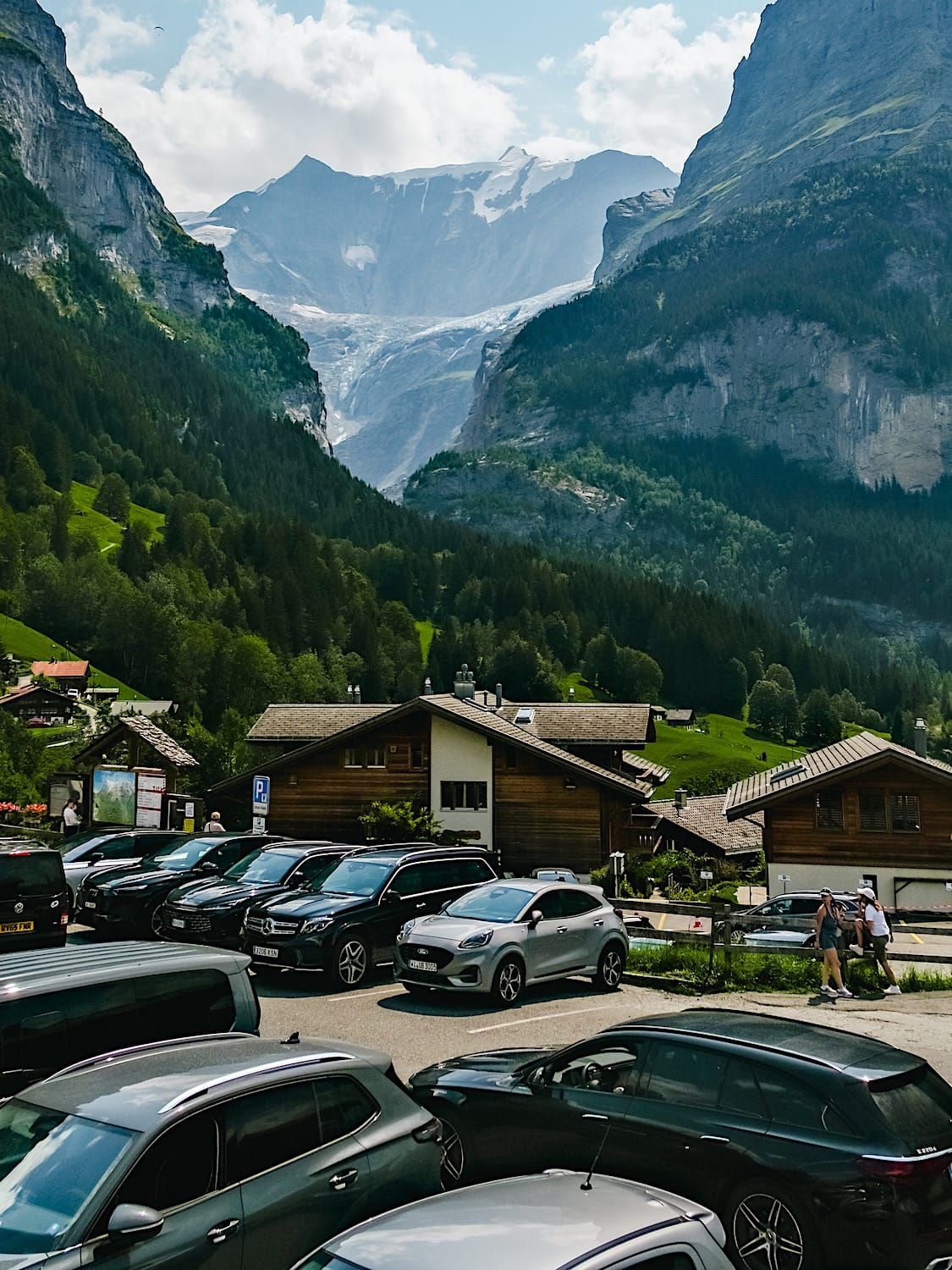 Wooden chalets and parked cars in Grindelwald with a glacier-topped mountain behind