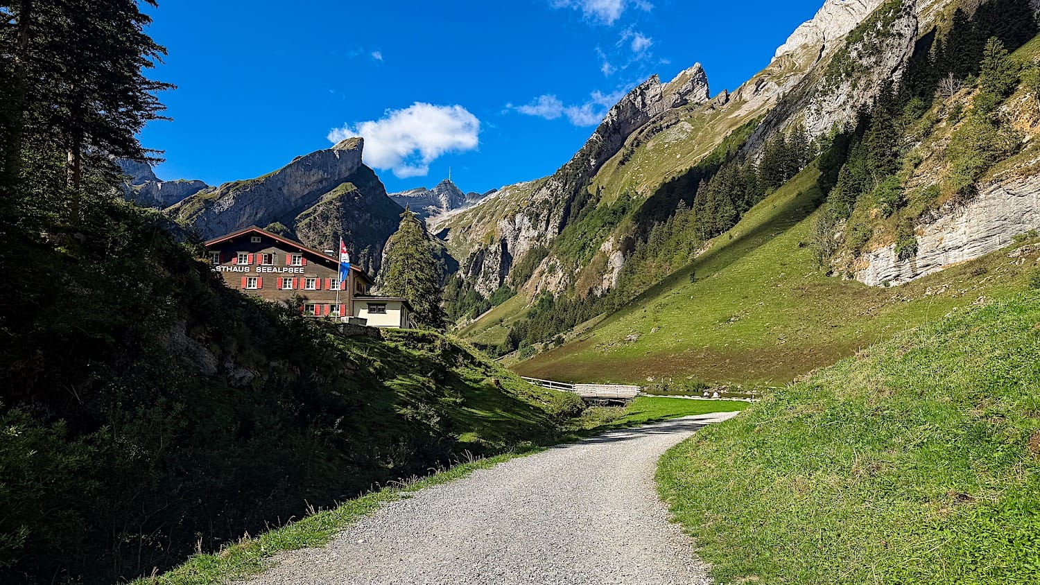 Gravel path climbing toward Berggasthaus Seealpsee, rocky peaks rising above the valley