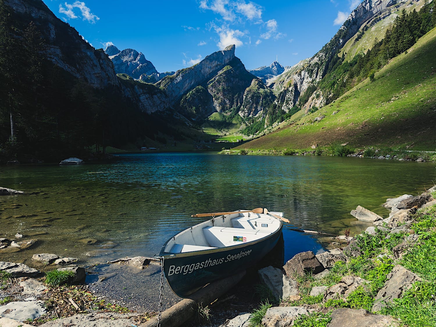 Rowboat marked "Berggasthaus Seealpsee" tied up at the shore of Seealpsee, mountains rising behind the lake