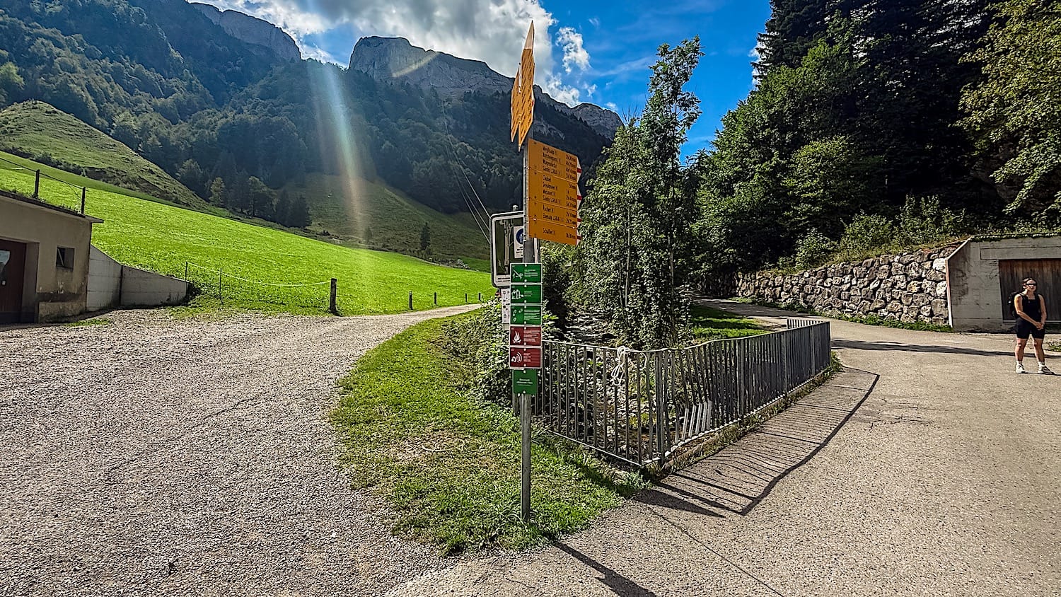 Yellow hiking signposts at the trailhead in Wasserauen, gravel service path leading up the valley