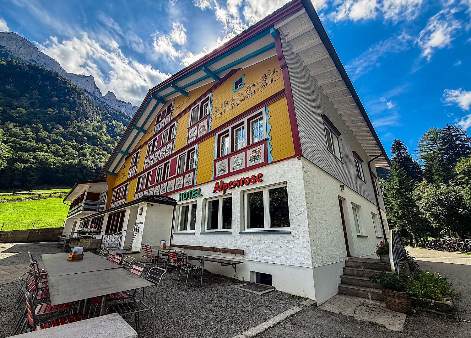 Yellow and red Hotel Alpenrose in Wasserauen with a terrace of tables out front