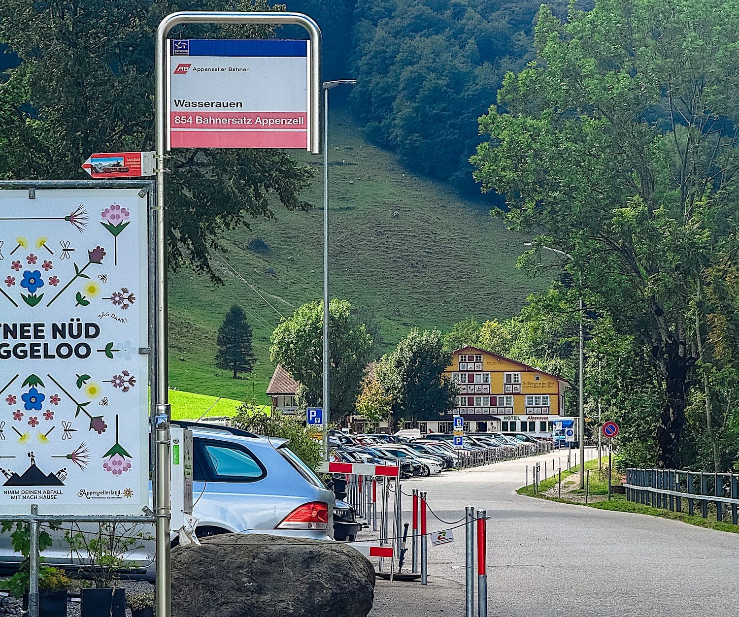 Wasserauen bus stop sign, with a parking lot and Hotel Alpenrose in the background