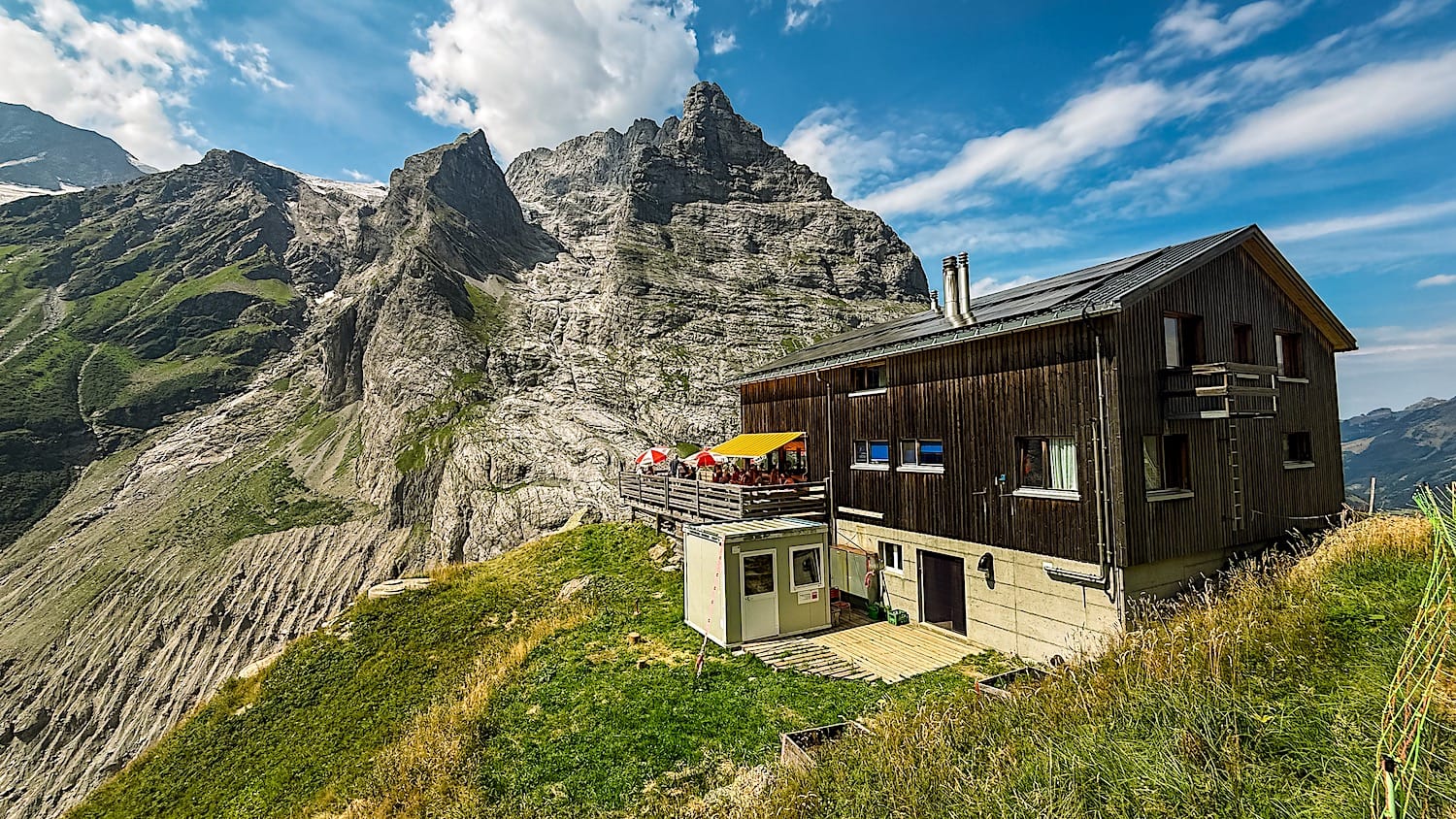 Bäregg Hut on a grassy ridge below jagged peaks and the glacier