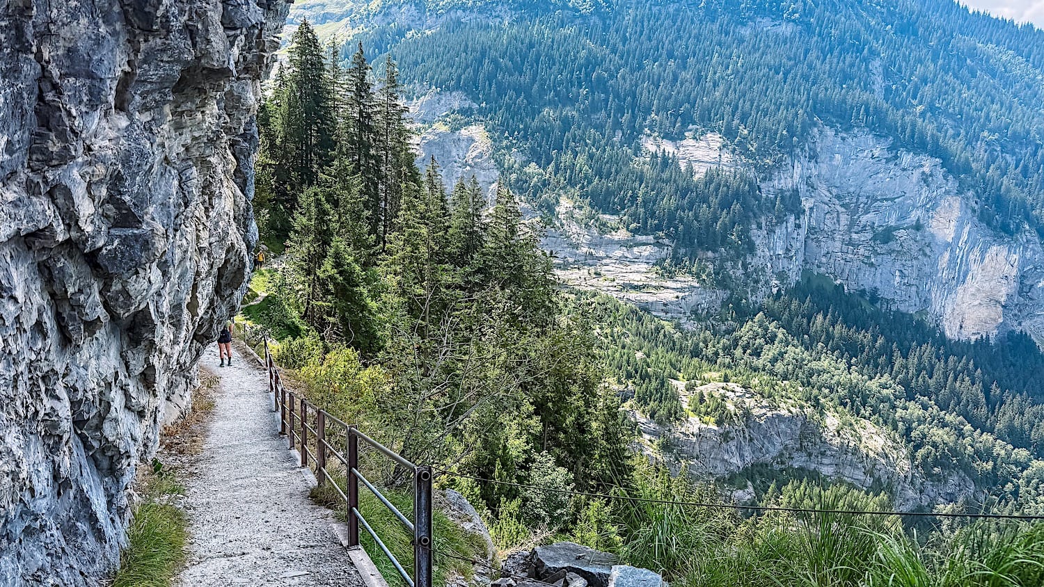 Paved path with a railing along a cliff at the start of the trail from Pfingstegg