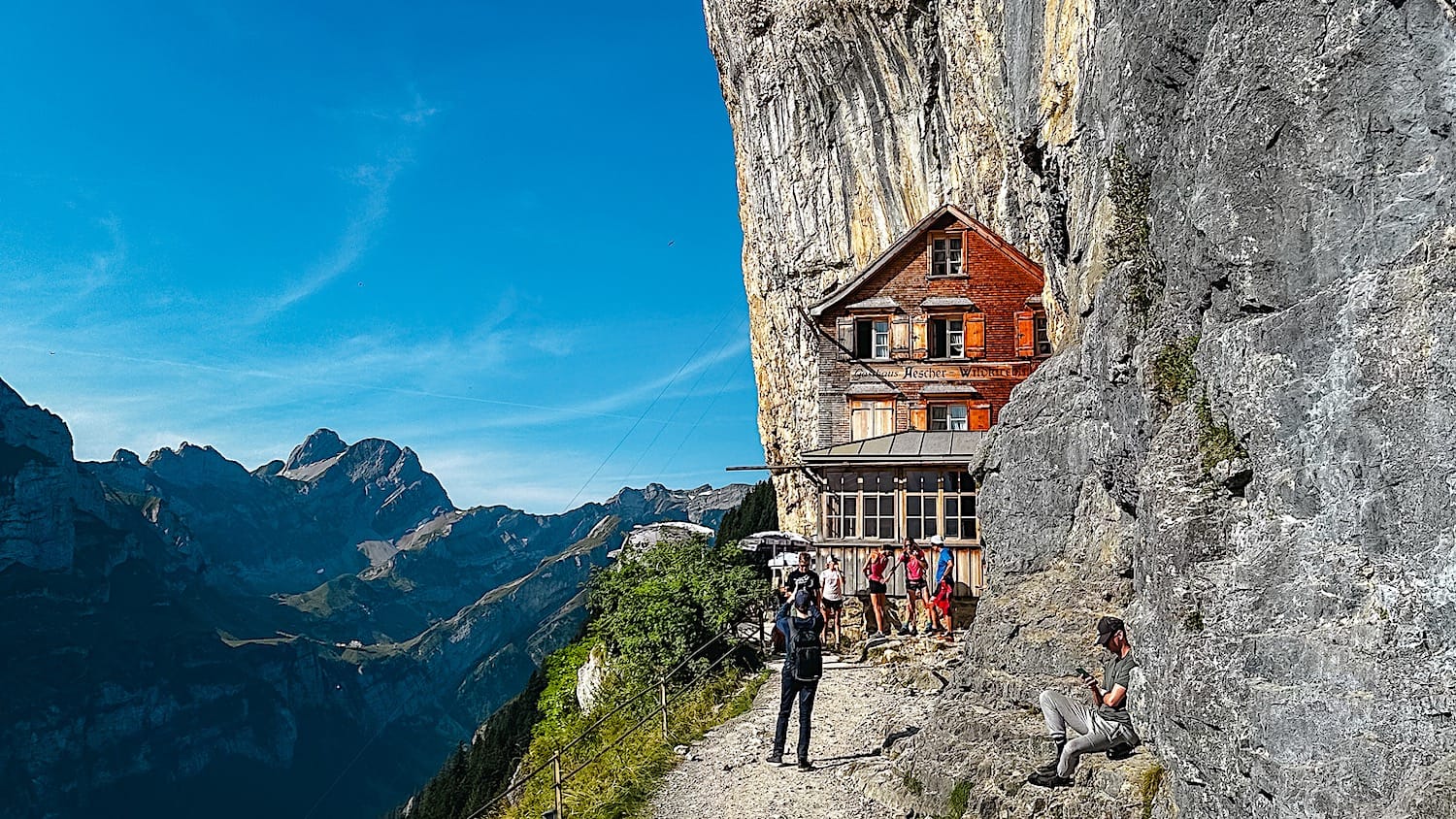 Berggasthaus Äscher built into the base of a vertical cliff, hikers gathered outside on the trail
