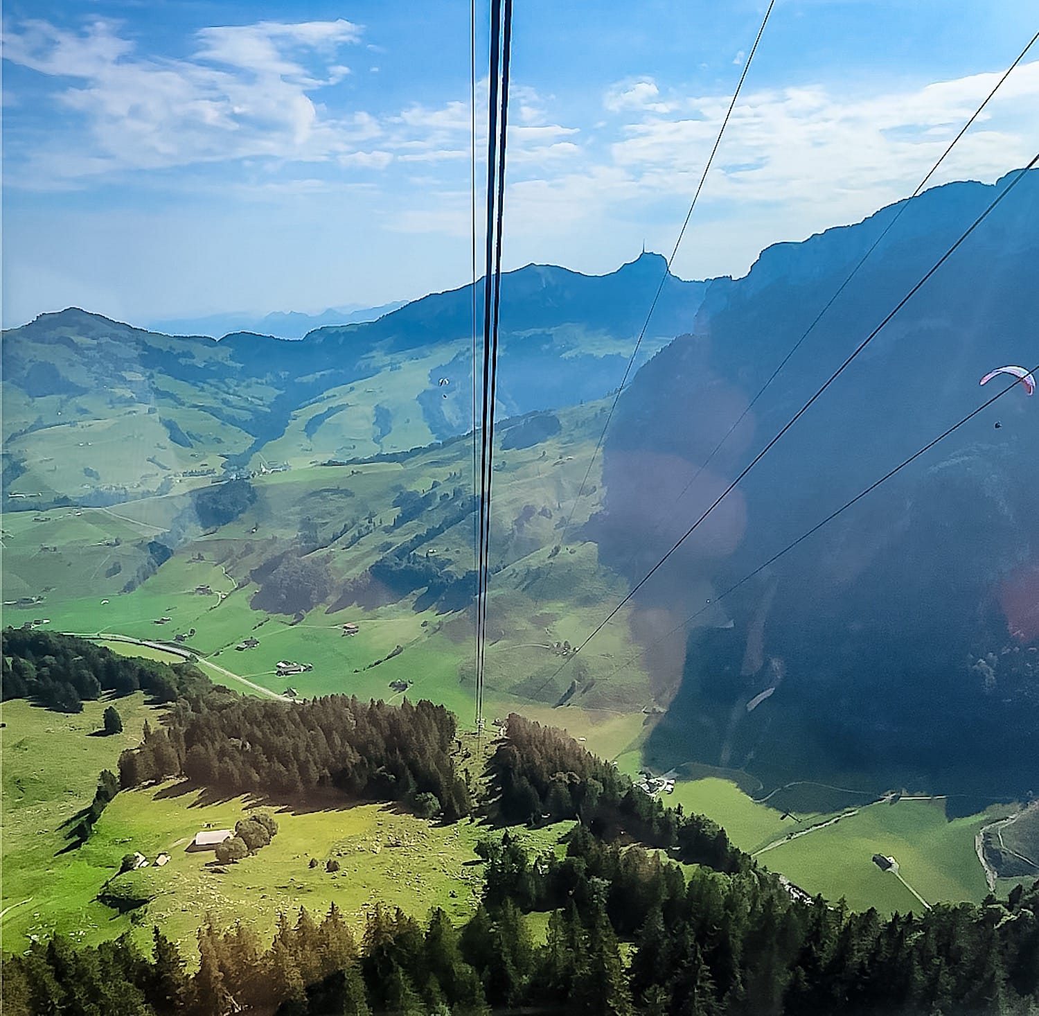View down the valley from the Ebenalp cable car, cables in the foreground and a paraglider at right