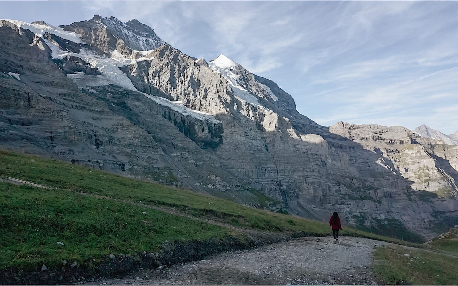 Hiker walking along the gravel trail below the rocky Eiger and its glacier