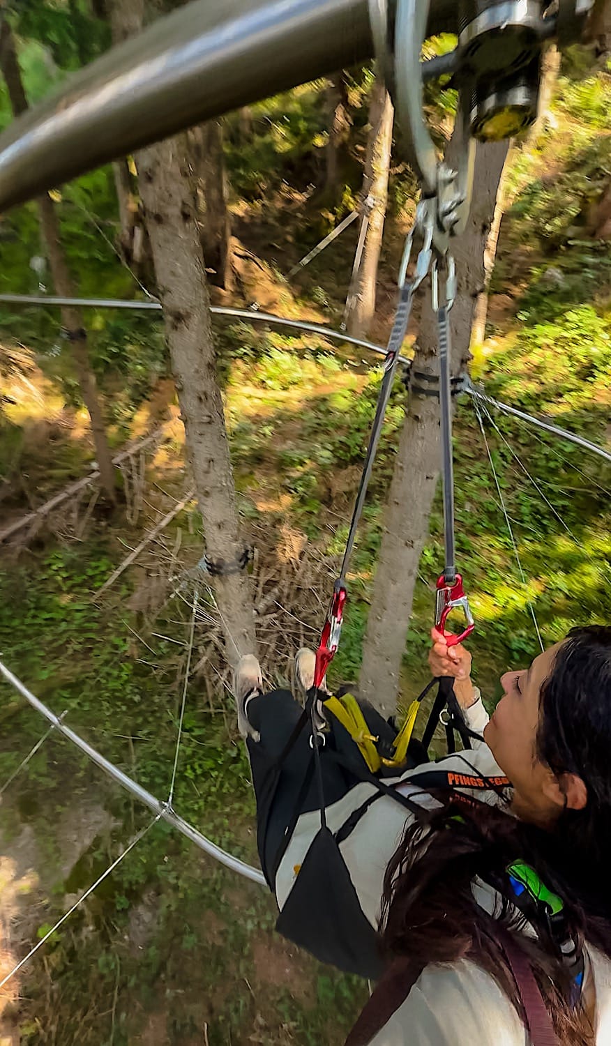 Woman in a harness riding the Pfingstegg Fly Line through the trees