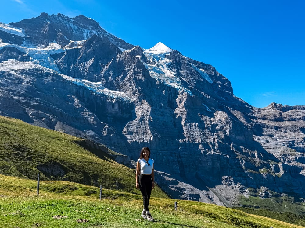  Hiker standing on a green slope below the Eiger and the Eiger Glacier